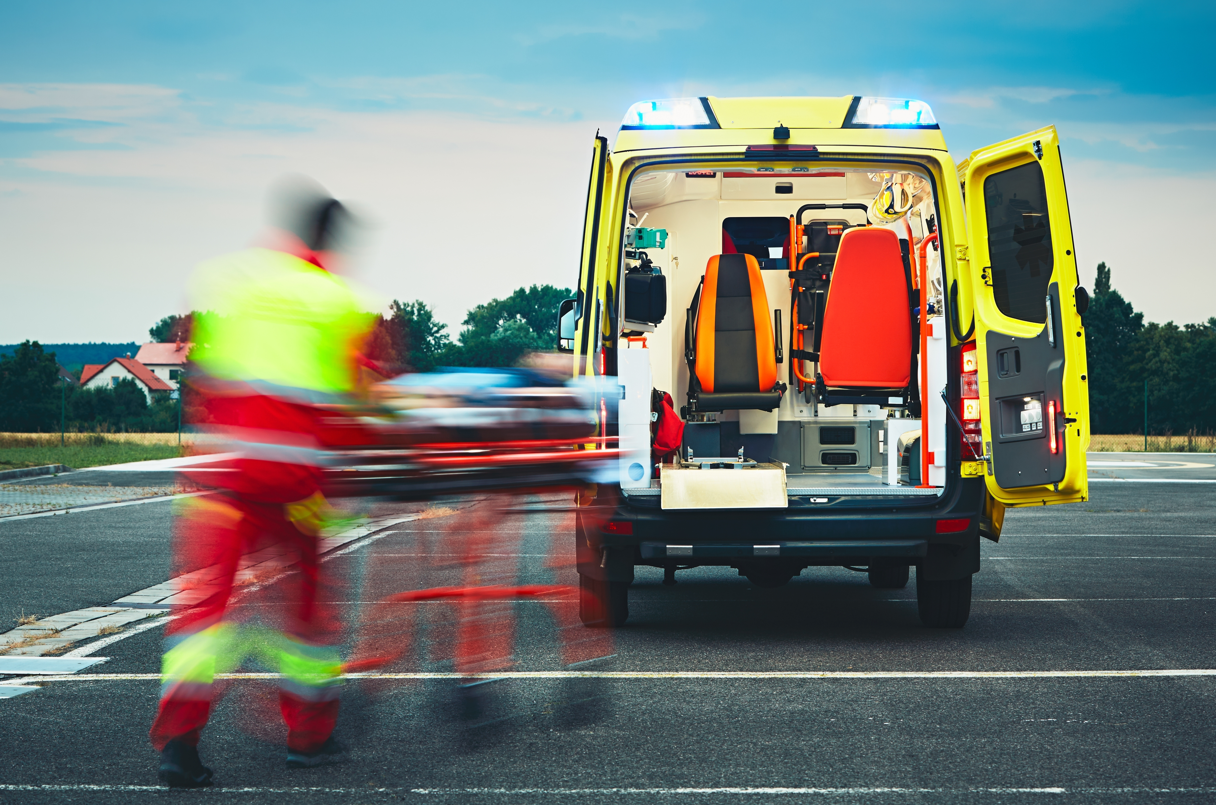 Un hombre con uniforme rojo y amarillo corre hacia la parte trasera de una ambulancia