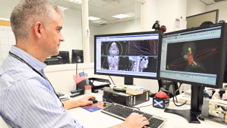 Señor sentado delante de dos pantallas de ordenador con imágenes 3D de partes del cuerpo humano