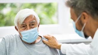 paciente hombre mayor sentado de frente a médico que aparece en lateral sentado poniendo una mano sobre su hombro