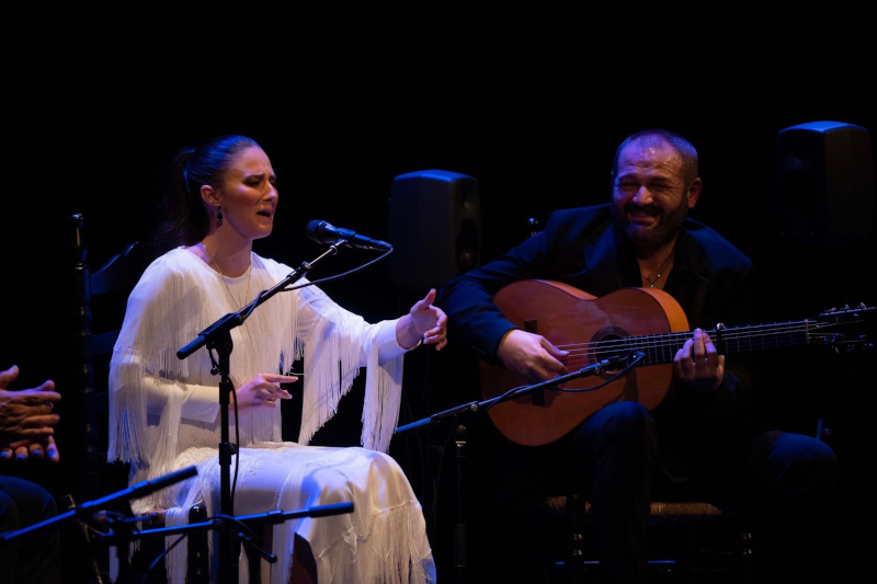 imagen de Lucía Beltrán con vestido blanco cantando, a su lado Patrocinio hijo tocando la guitarra