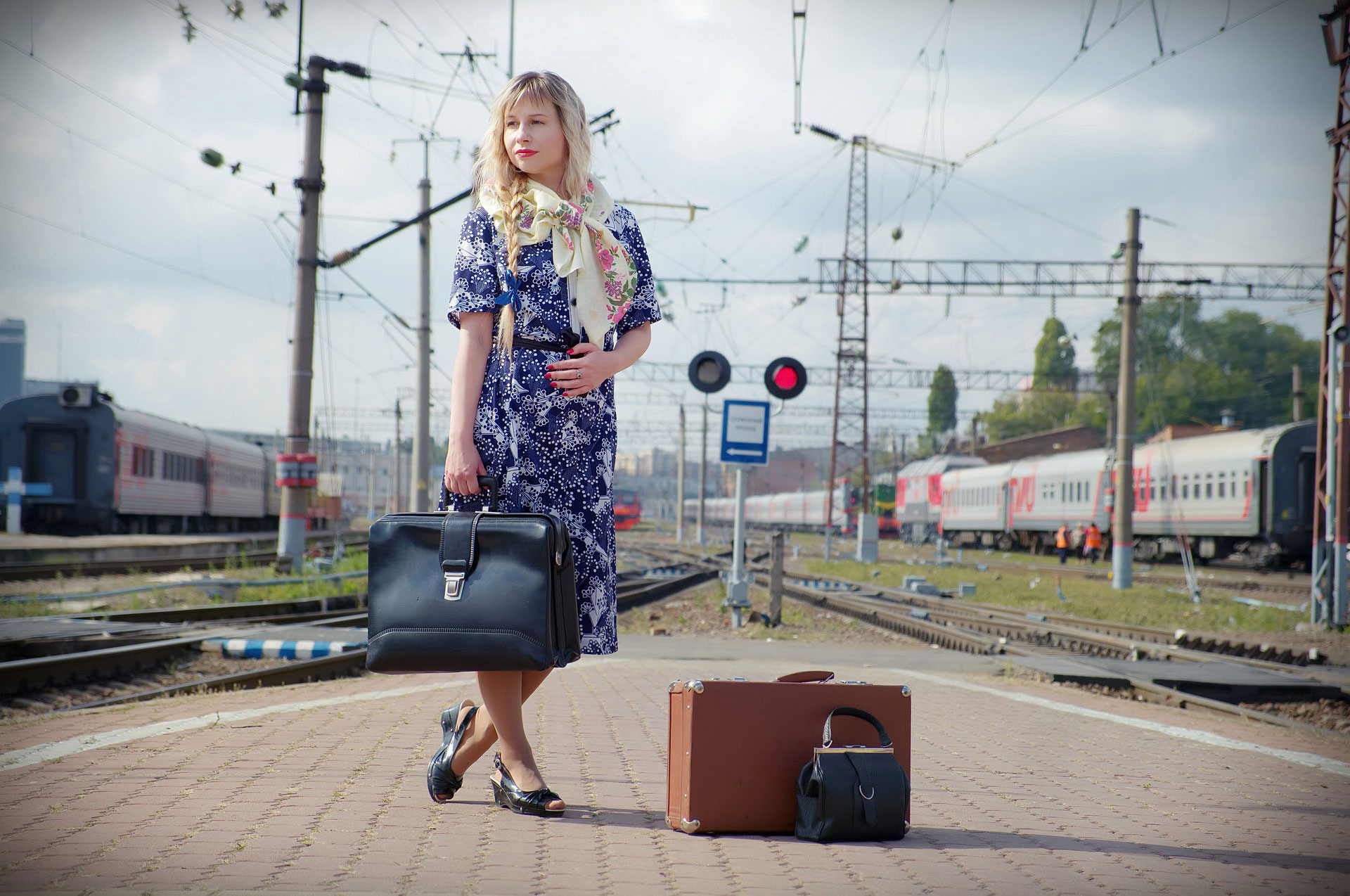 Mujer de pe en un anden ferroviario, con una maleta en la mano y otra a los pies