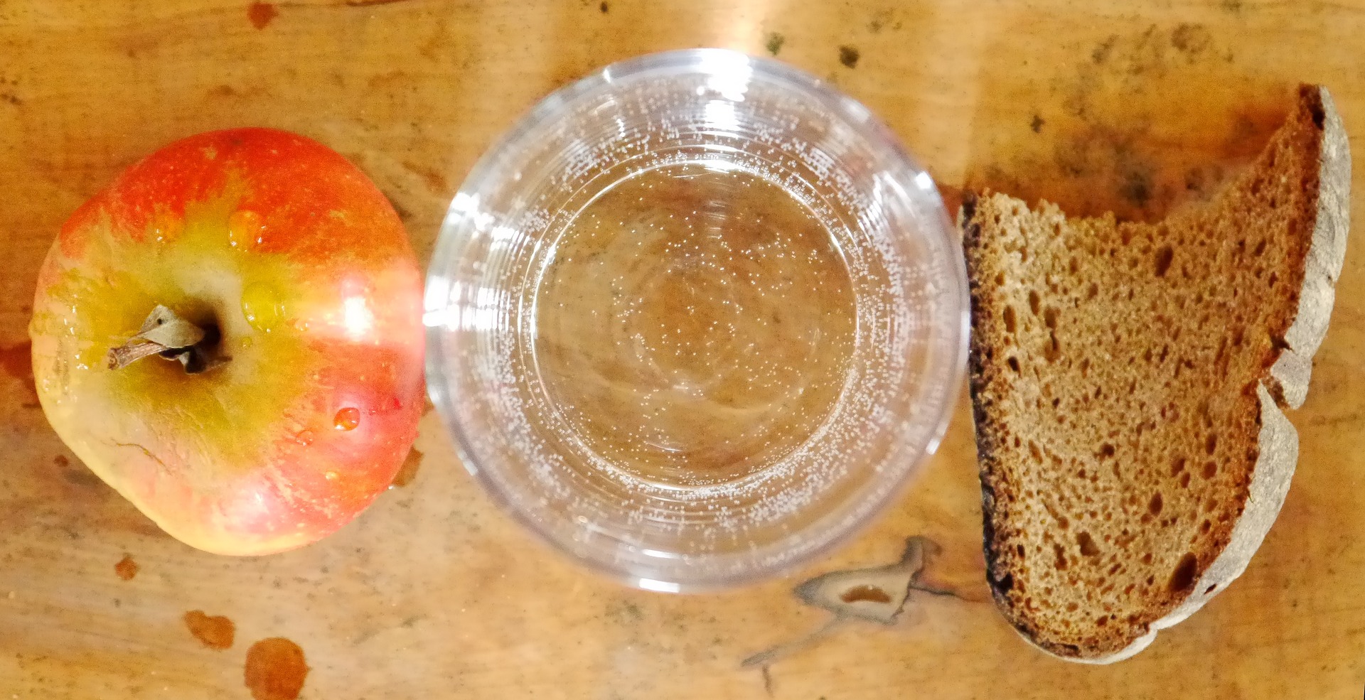 una manzana, un vaso de agua y un trozo de pan sobre una mesa
