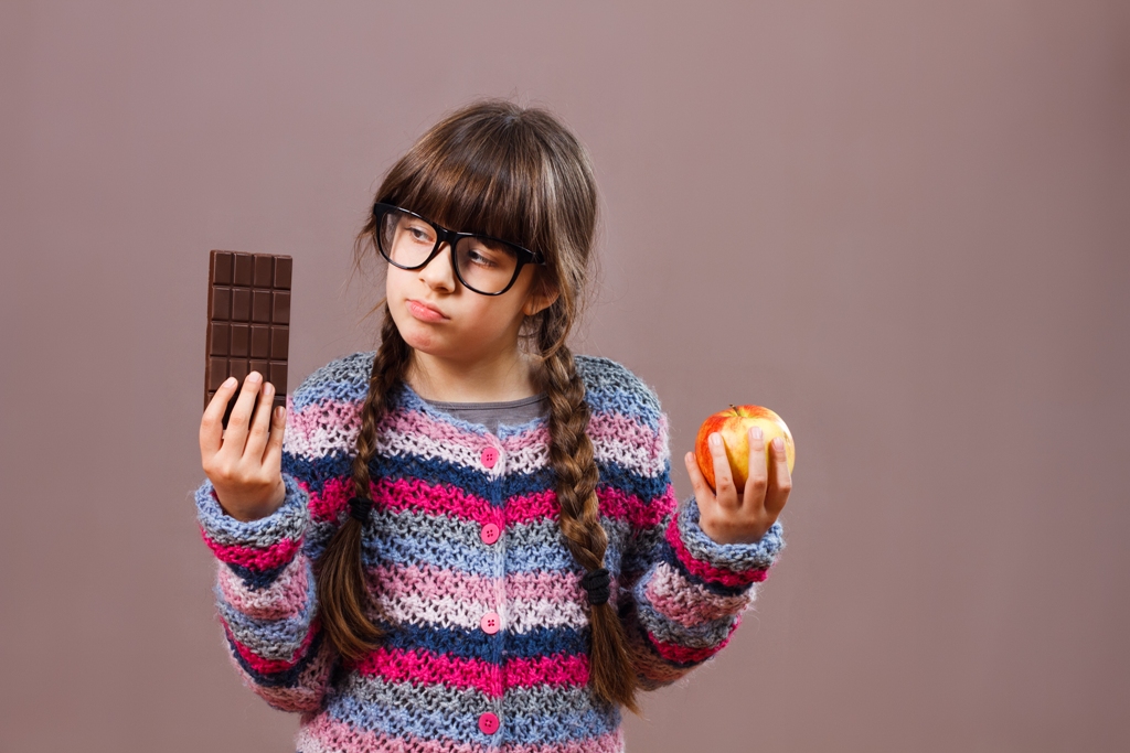 niña dudando entre tableta de chocolate y manzana