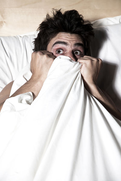 hombre con cara de miedo en la cama tapándose la cara con las sábanas