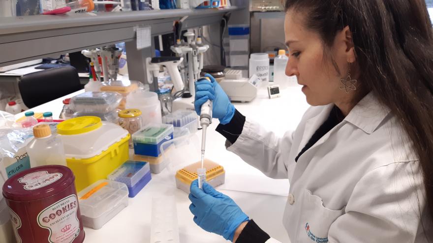 mujer con bata blanca de lado pipeteando en un laboratorio