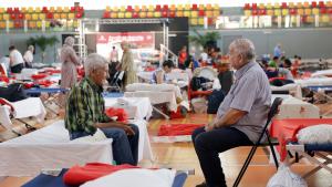 Díaz Ayuso anuncia una inversión de 10 millones de euros para reforzar el cuidado a las familias con necesidades especiales de la Sierra Oeste Señores sentados en el pabellón de un polideportivo tras ser evacuados de sus casas