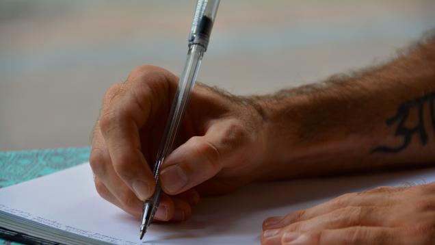 Detalle de las manos de un hombre escribiendo a bolígrafo en un libro de registros