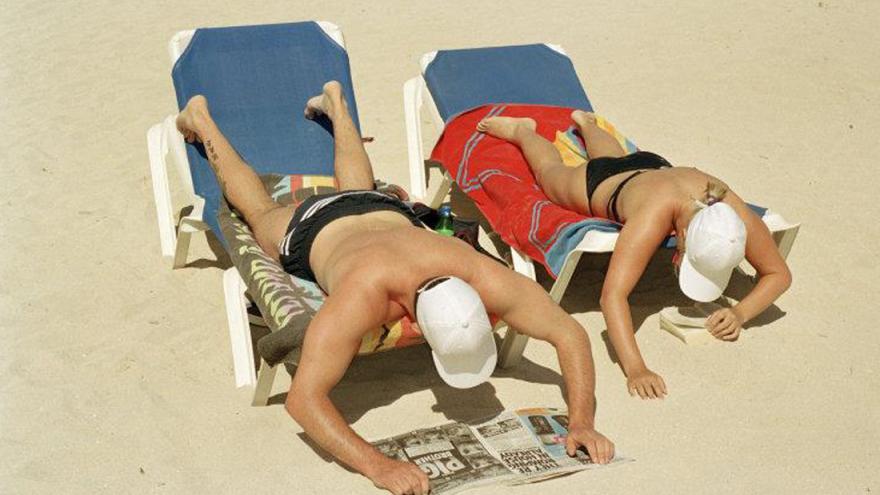 Hombre y mujer leyendo y tumbados boca abajo en la playa