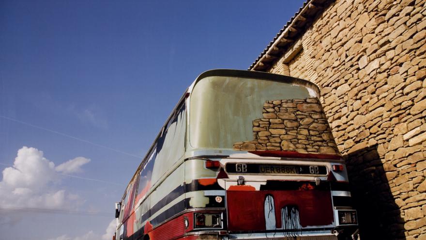 Autobús rojo apoyado en una tapia de piedra