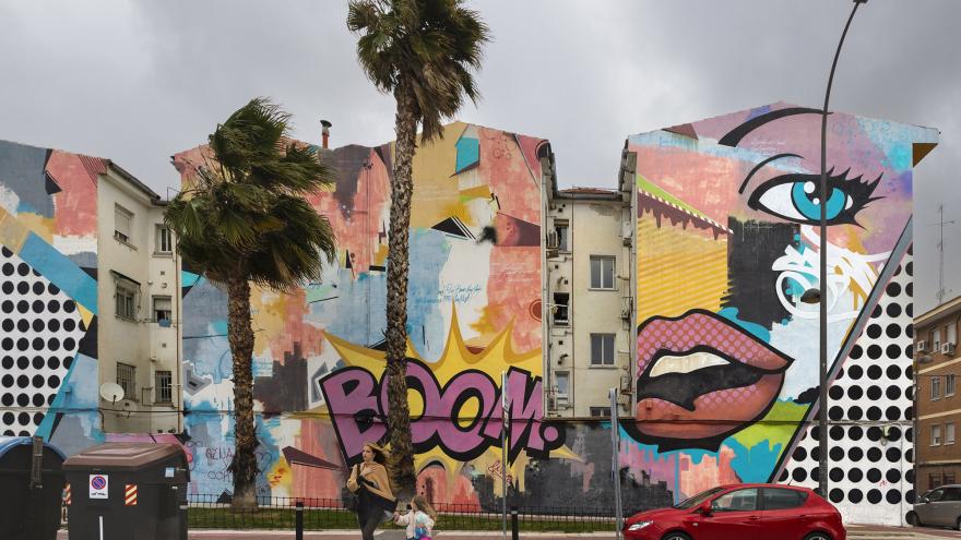 Calle de una ciudad con edificios con grafitis, palmeras y coche rojo