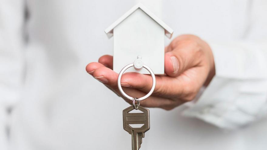 Una mano sostiene una maqueta de una casa y una llave