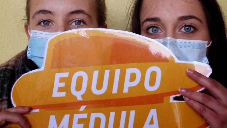 dos chicas con un cartel del escudo de equipo médula delante de la cara dejando ver sus ojos