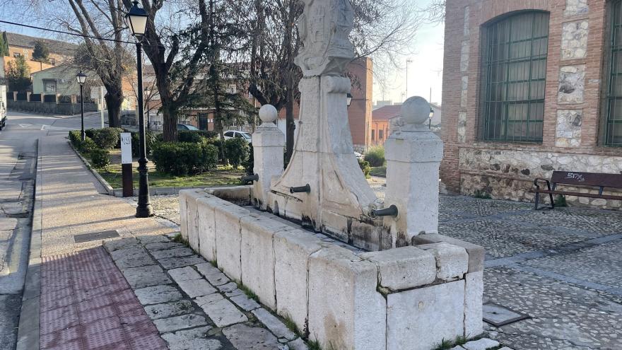 White stone fountain with a water basin, two columns and a central shield with inscriptions