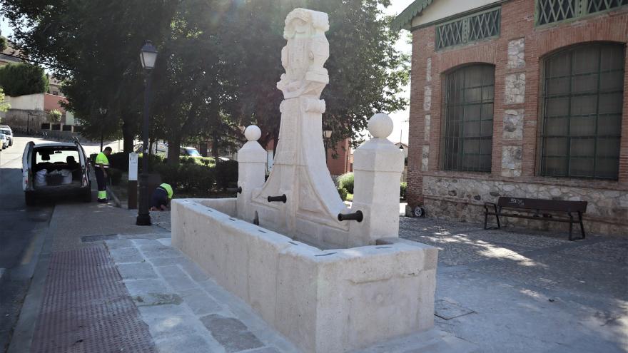 Frontal image of a white stone fountain with two side columns, front shield with inscriptions and water basin