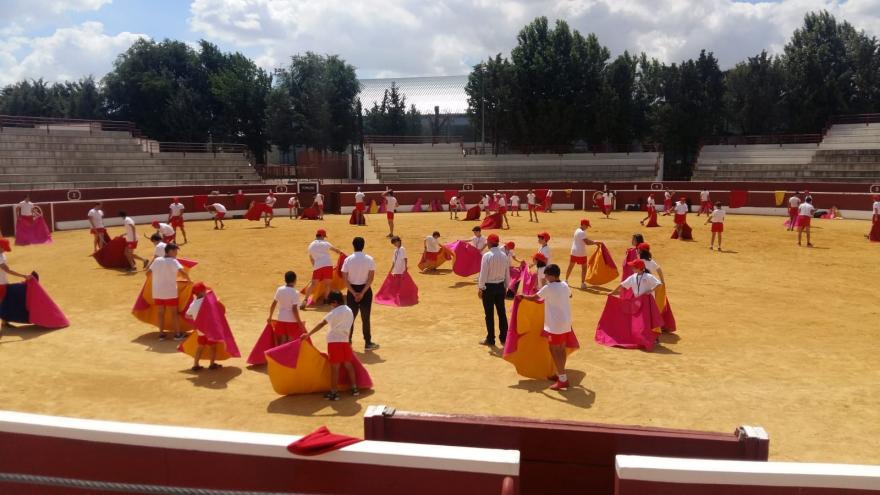 Niños y niñas de entre 8 y 14 años con capote en el albero de una plaza de toros aprendiendo a torear