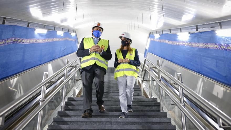 El consejero junto a la responsable con chaleco y casco de obra bajando las escaleras de la estación de Metro de Madrid