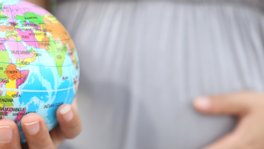 tripa de mujer embarazada que sostiene en su mano una bola del mundo