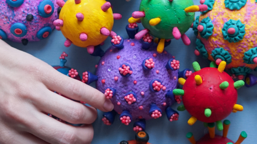 virus del covid en modelos 3D de colores al lado de una mano