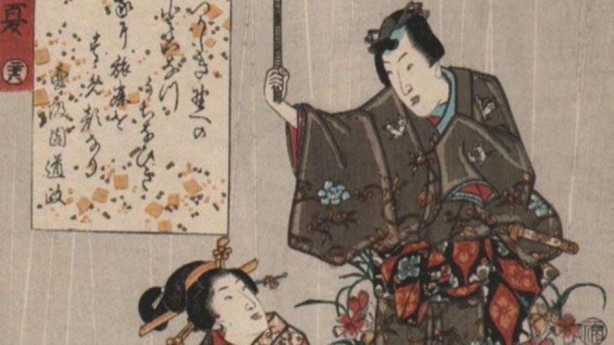 Hombre japonés cubre con sombrilla a una mujer agachada, los dos con trajes típicos