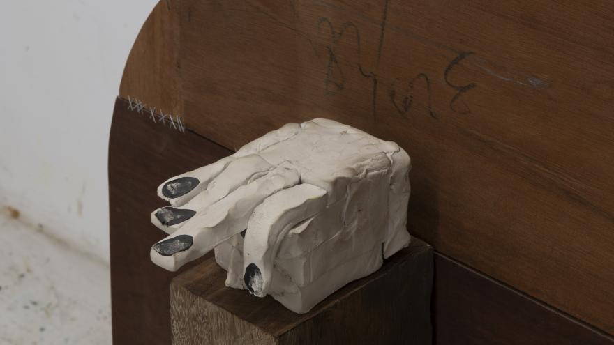 Imagen de una mano en escayola blanca sobre un banco de madera oscuro