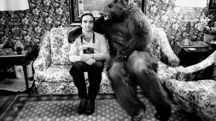 Hombre sentado en un salón junto a un gran oso