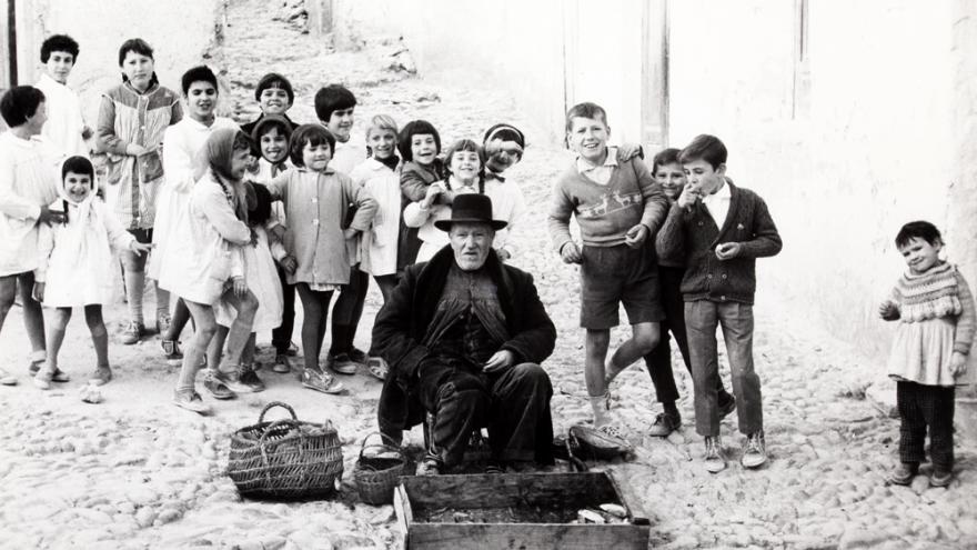 Man with hat sitting on the street surrounded by children