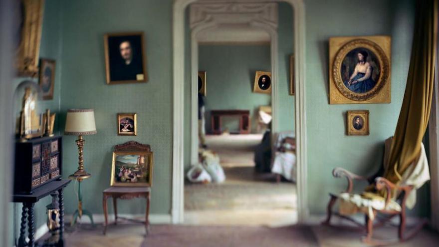 Interior de una casa antigua con mobiliario envejecido y paredes en color verde llenas de lienzos enmarcados con cuadros del siglo XIX