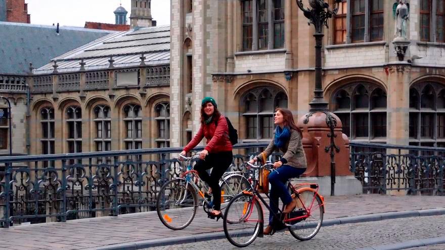 Two girls ride a bike through a city
