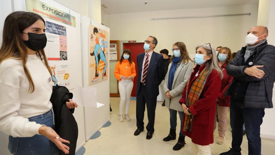 Responsables de Centro de Transfusión, Hospital del Henares, Ayuntamiento de Coslada escuchando a alumna que explica junto a exposición