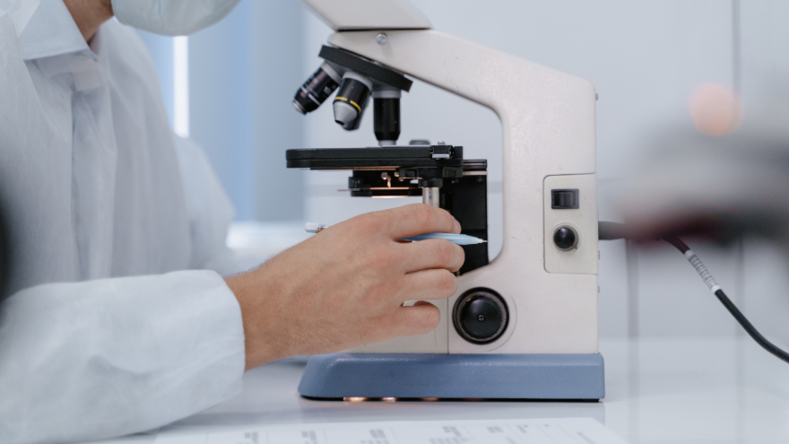 Mano de hombre con bata blanca sobre un microscopio que ocupa casi toda la imagen