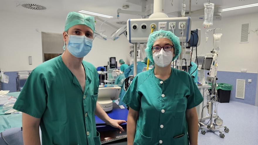 un cirujano y una cirujana posando delante de la mesa de operaciones en quirófano