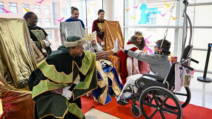 Un niño en silla de ruedas choca la mano con los Reyes Magos