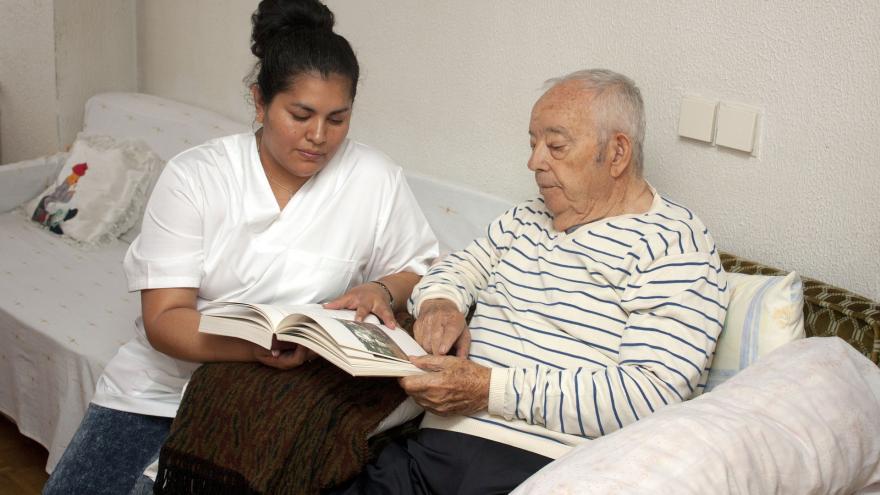 Mujer joven sentada junto a hombre mayor mirando un libro