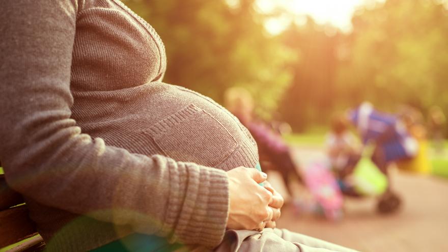 Una joven embarazada toca su barriga sentada en un parque