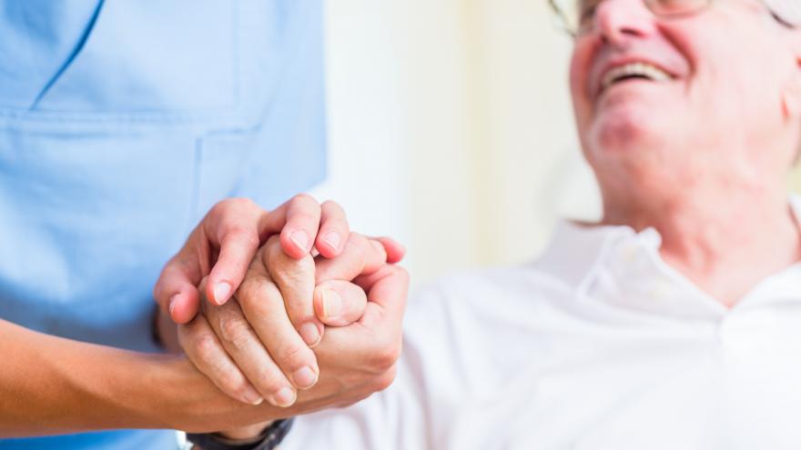 Una enfermera coge la mano de un anciano que le responde con una sonrisa