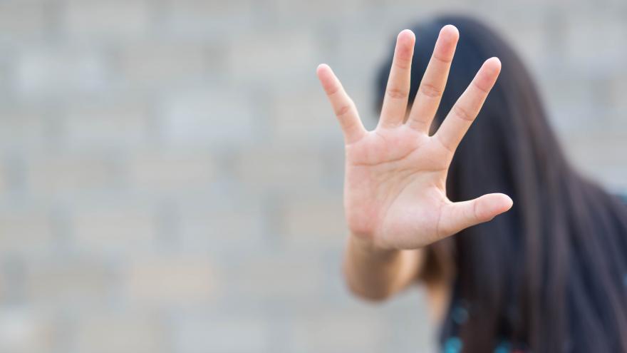 Una mujer se tapa la cara con la mano extendida hacia la camara