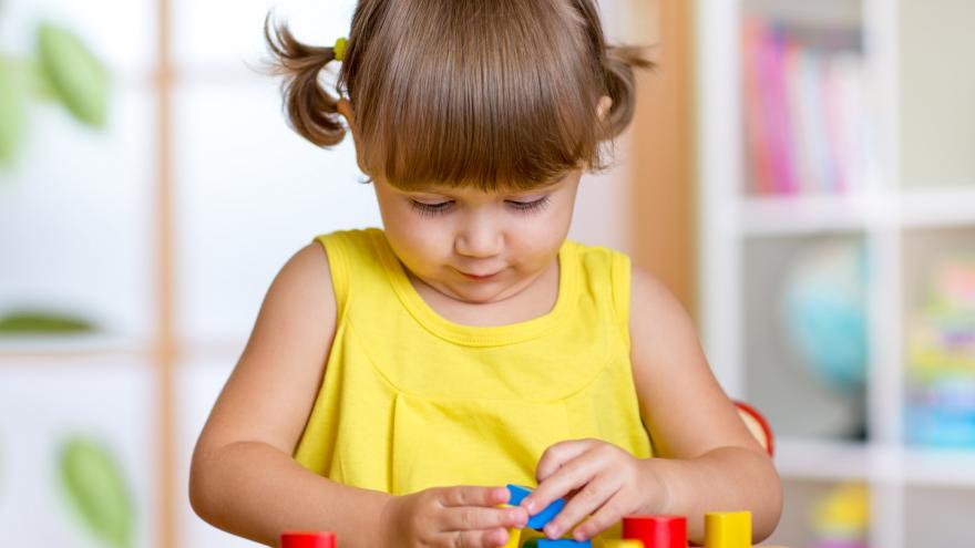 Niña pequeña encajando concentrada piezas geométricas de madera