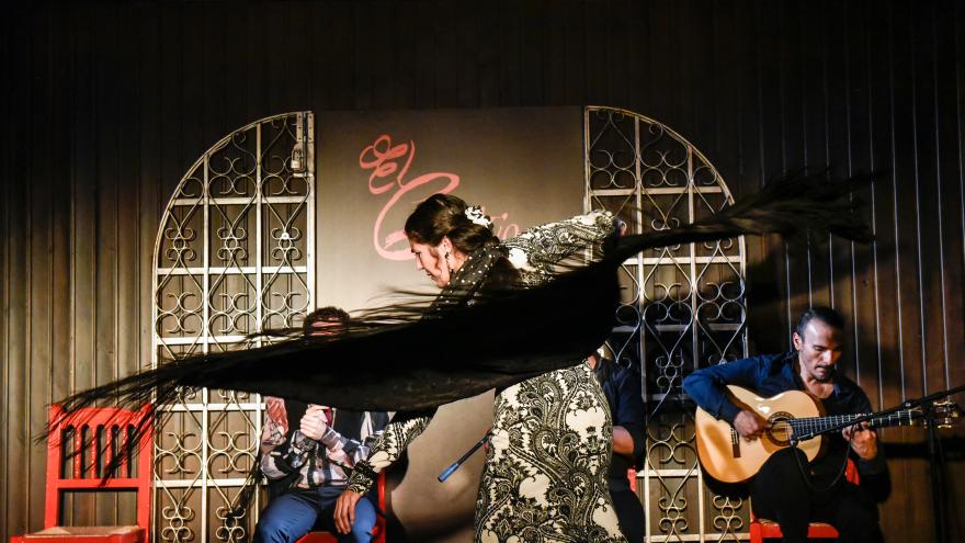 Mujer bailando flamenco en un tablao y músicos al fondo