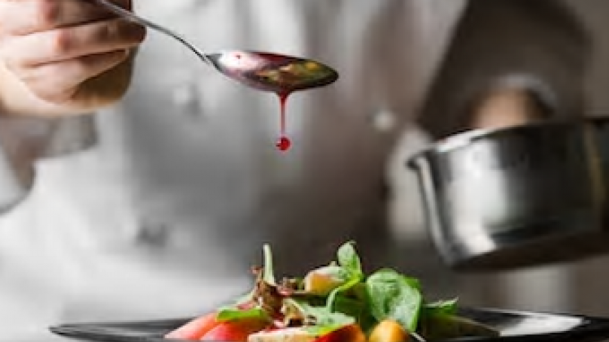 Plato de comida sobre el que cae una gota de salsa de una cuchara, fondo torso de cocinero