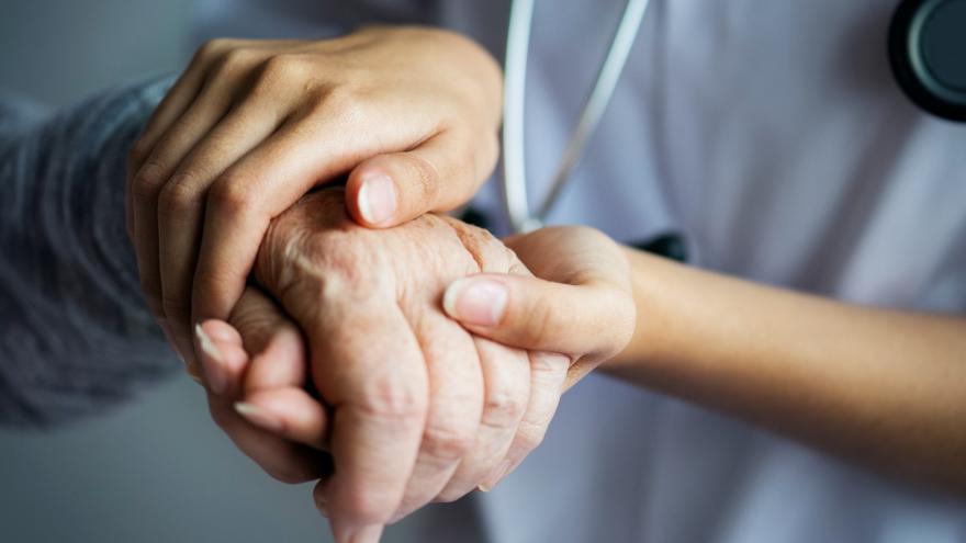Un sanitario coge las manos de una persona mayor