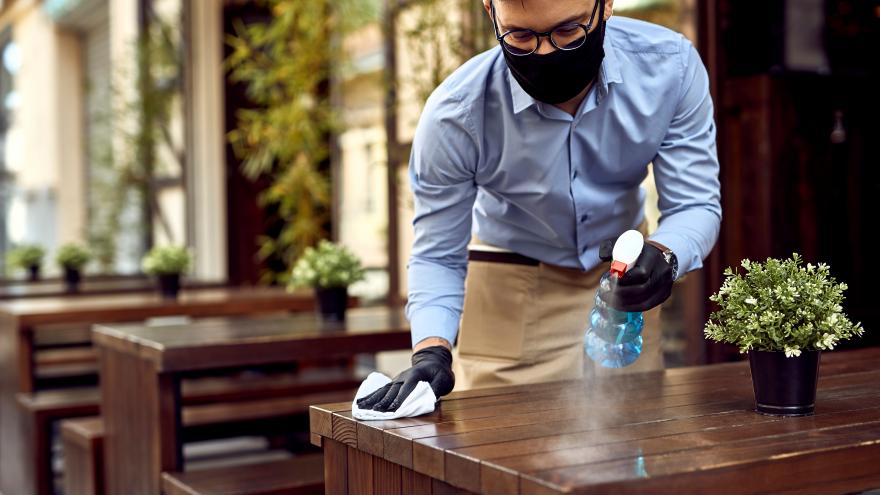 Un camarero con mascarilla desinfecta la mesa de la terraza