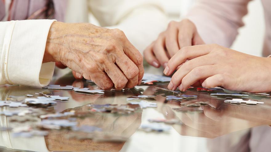 Las manos de unas personas mayores jugando un juego de mesa en una residencia