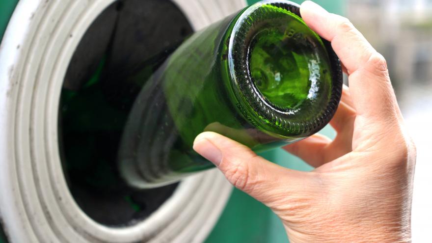 Una mano metiendo una botella verde en un cubo de reciclaje 