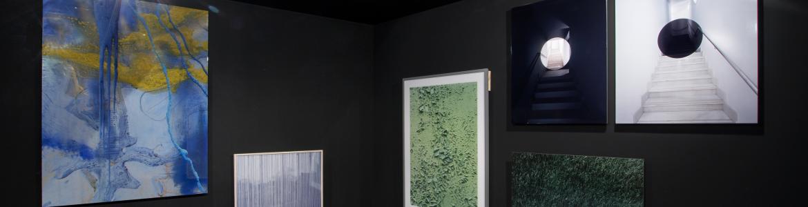 Vista de una exposición con paredes oscuras y varios lienzos colgados en ellas