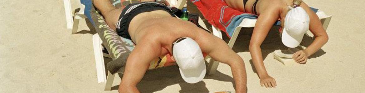 Hombre y mujer leyendo y tumbados boca abajo en la playa