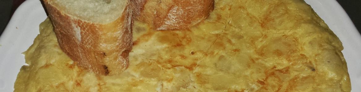 Tortilla de patatas en un plato con un triángulo cortado y dos trozos de pan encima