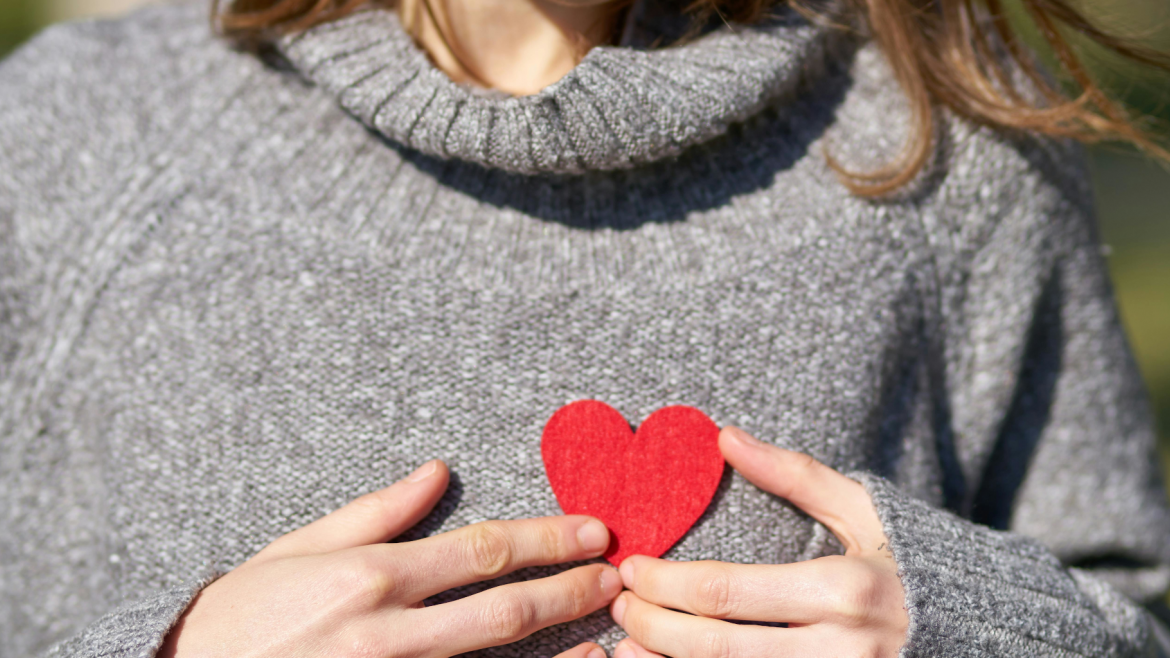 Imagen de un corazón de cartón rojo sobre ropa abrazado por dos manos