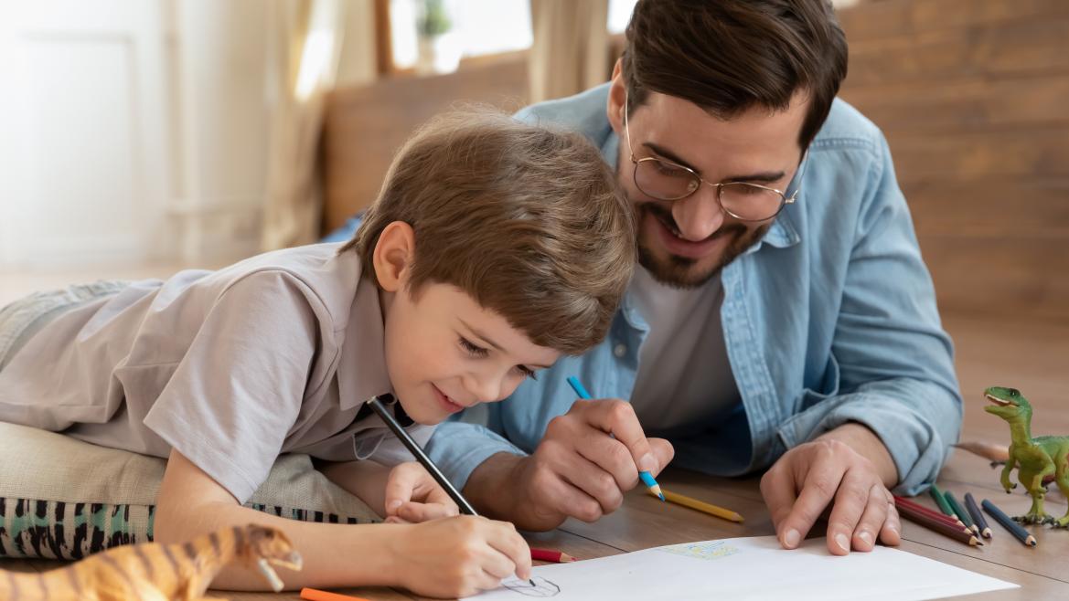 Niño y padre escribiendo en unos papeles en el suelo