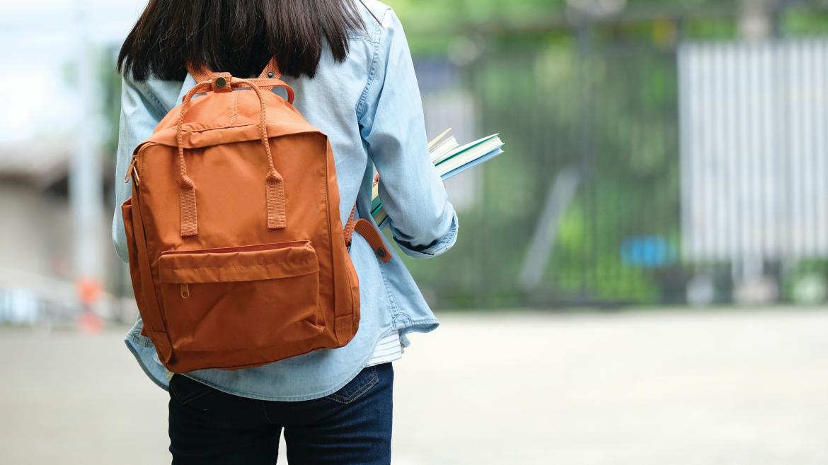 Chica joven caminando con una mochila a su espalda y libros en las manos