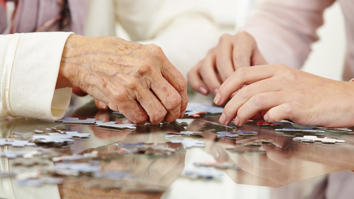 Manos de una persona mayor resolviendo un puzzle en una residencia_